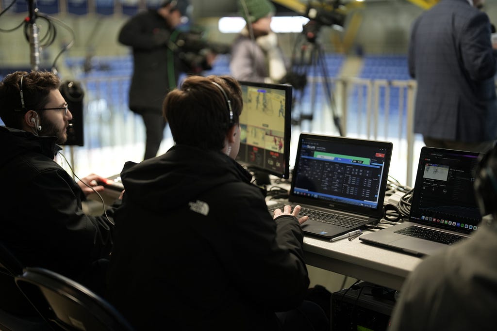 Two technicians operate computers during a livestream broadcast.