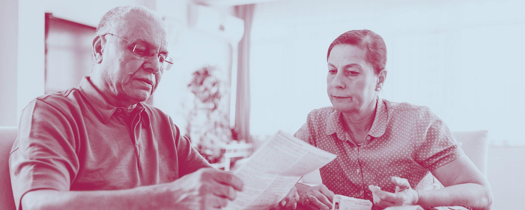 An older man and woman are sat together at a table looking at their bills.