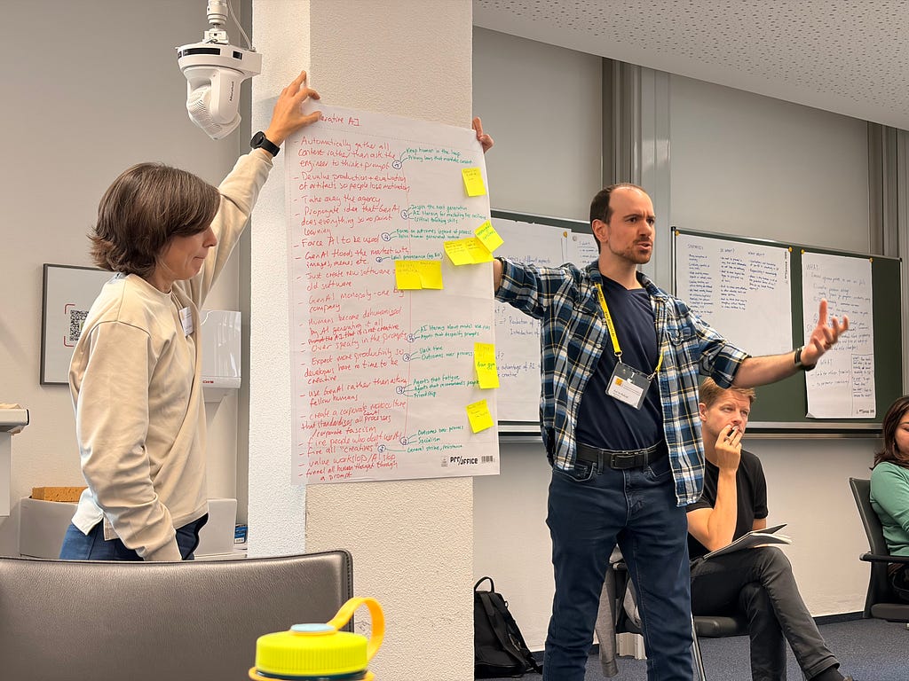 Karim gesturing while holding a poster on the wall with Victoria’s help. Red and green marker splattered about.