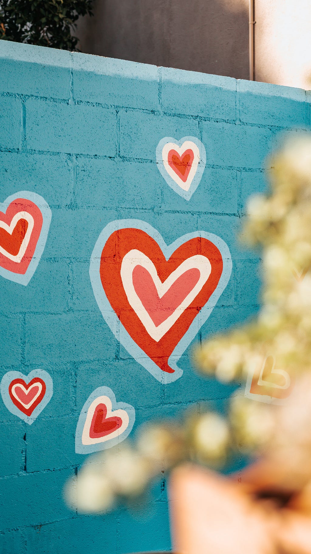 A turquoise wall with red hearts painted. Within each heart, there are different colors that make up smaller outlines of hearts