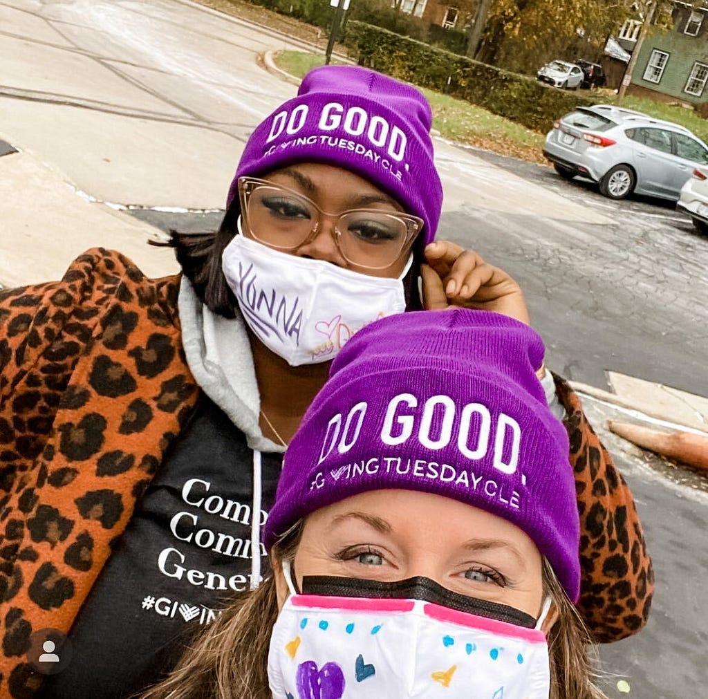 A white woman and a Black woman wearing purple winter hats that say Do Good GivingTuesday CLE hats in reference to Cleveland
