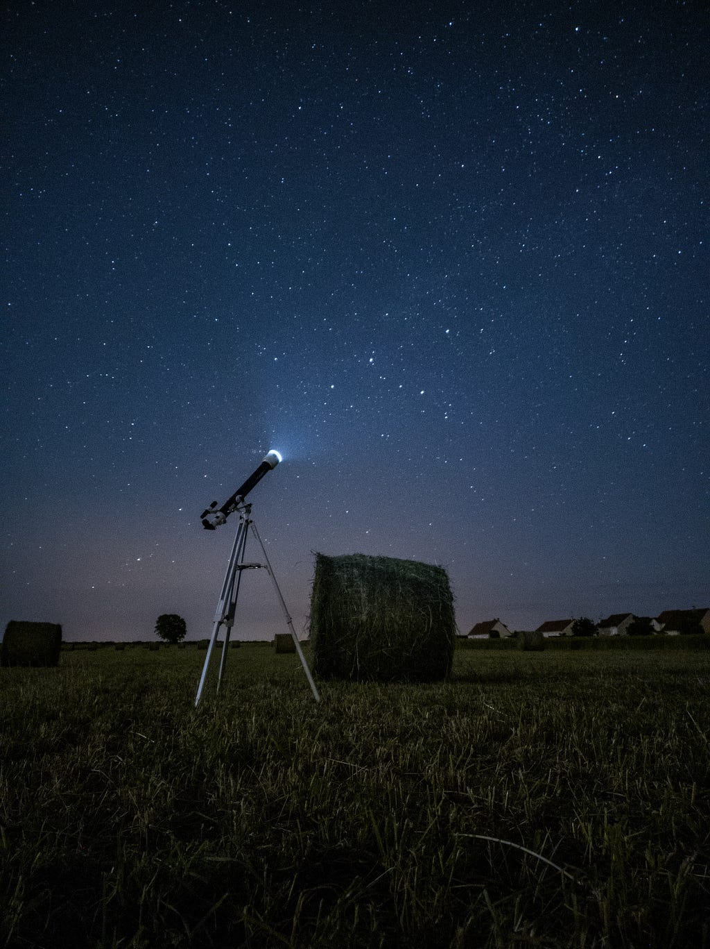 An image of a telescope in a field of hay bales at night. Photo by Simon Delalande on Unsplash.