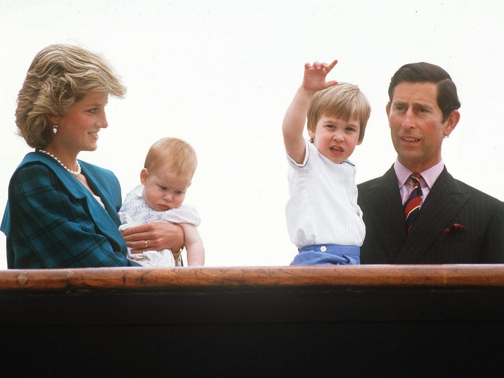 Diana, the Princess of Wales, holds her son Harry, while looking at Prince William, held by his father Prince Charles.