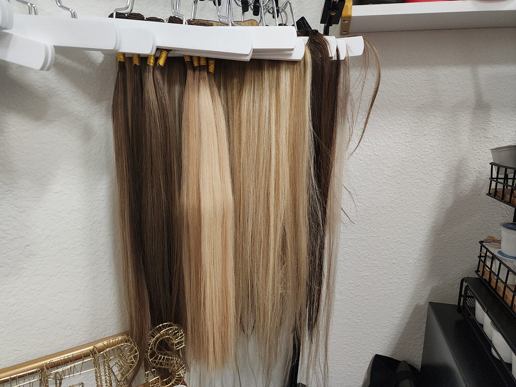 Blonde and brunette hair extensions hanging from hangers and rod.