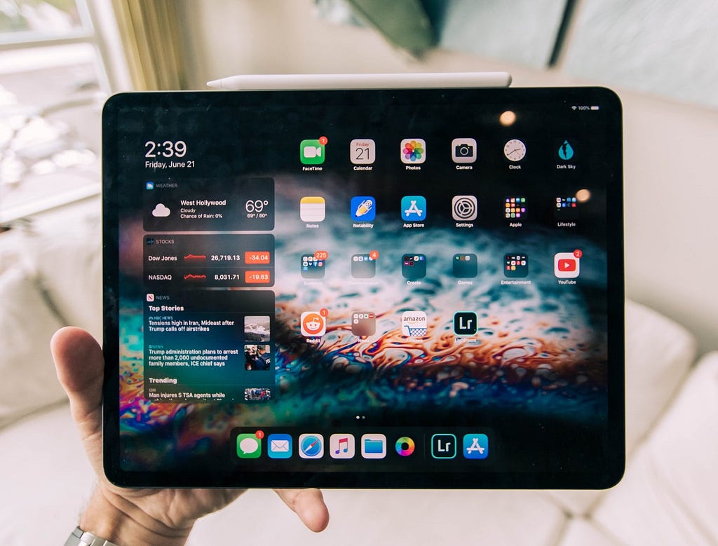 A hand holding an iPad pro with its screen lit with colorful app icons.