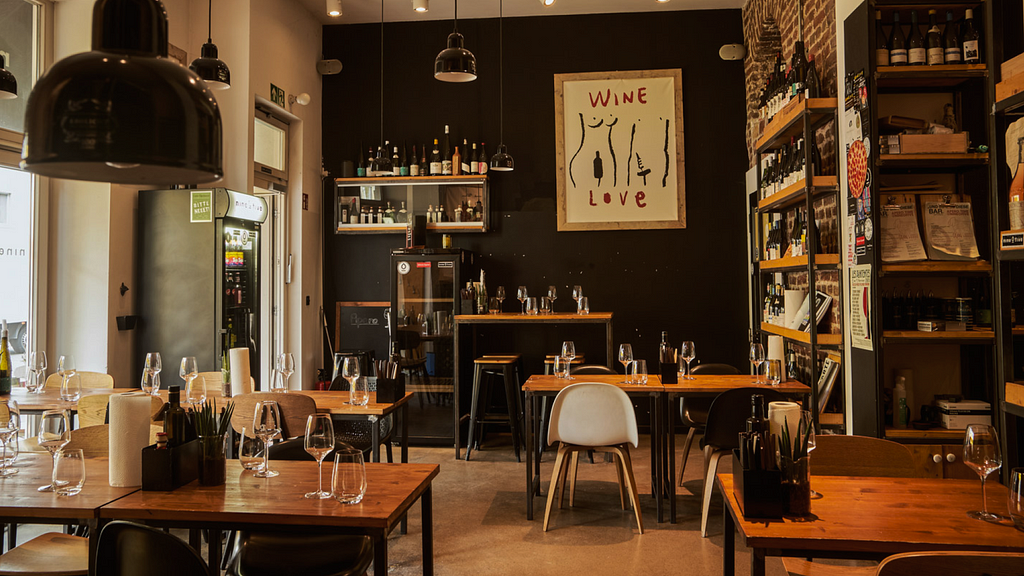 Shows a modern pizzeria with wooden tables and wine glasses.