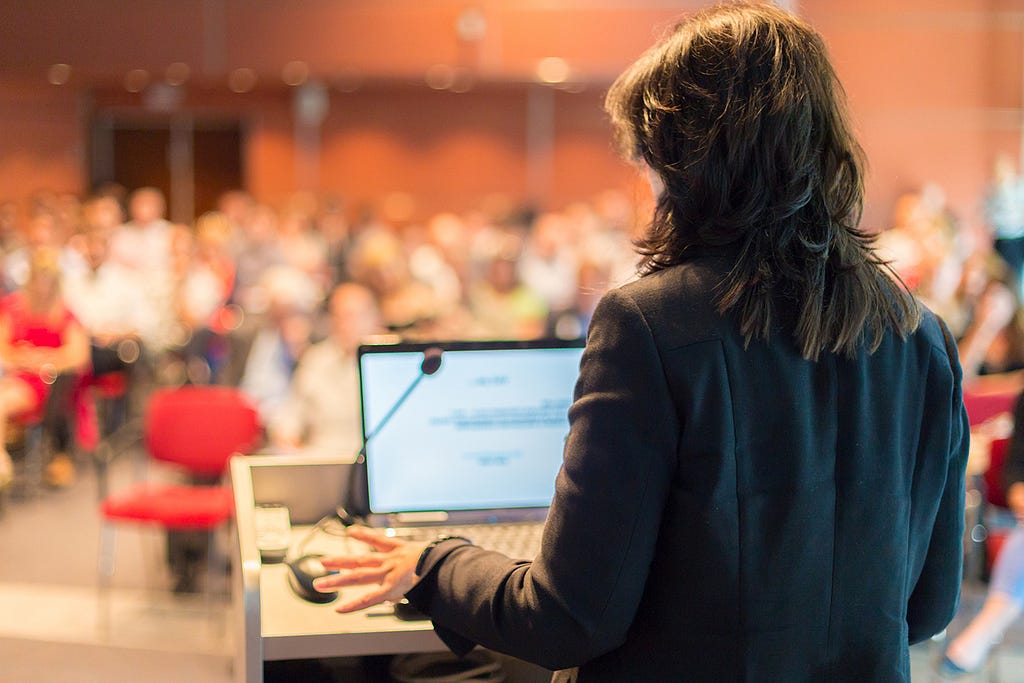 Imagery of researchers giving presentation to large room of people