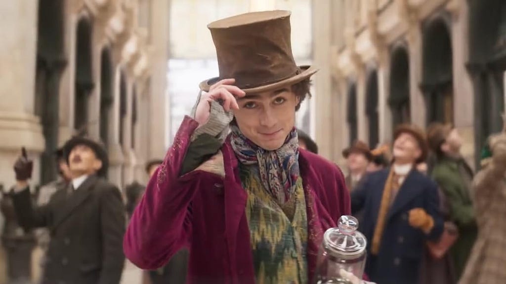 A screenshot from Wonka (2023). Willy Wonka tips his hat towards the camera.