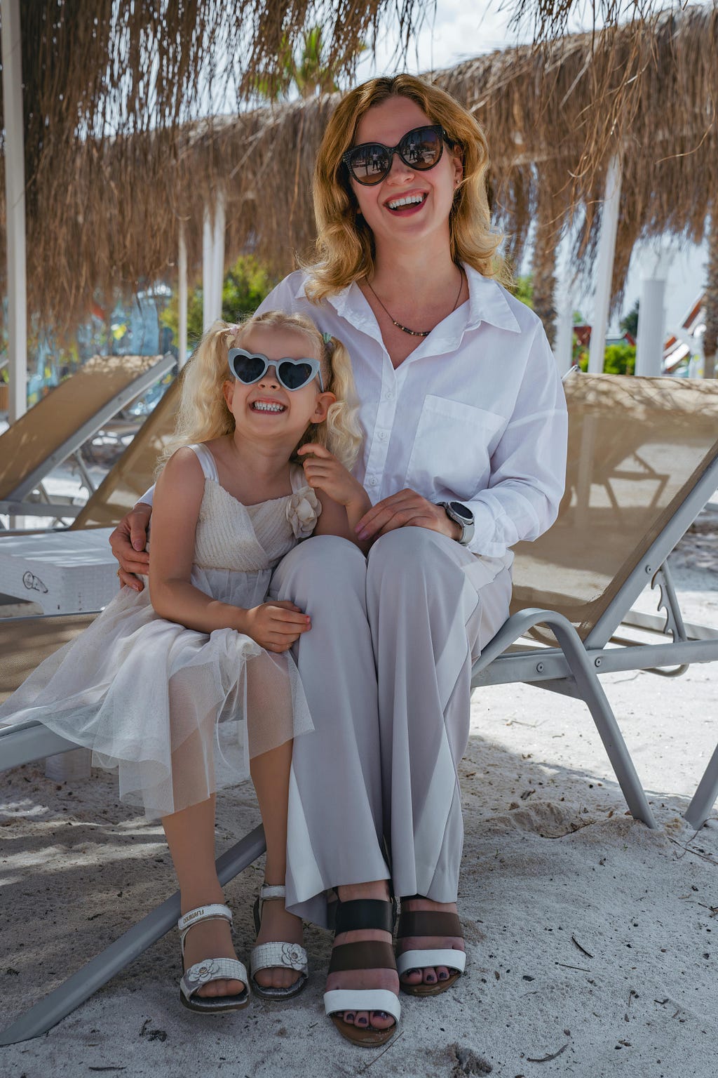A mother with a daughter sitting dressed in nice clothes on a chair at the beach.