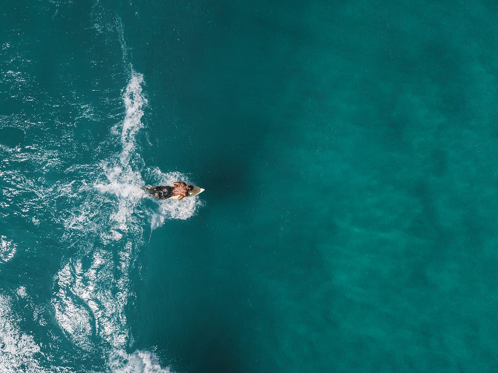 foto área de um rapaz deitado em uma prancha surfando uma onda pequena