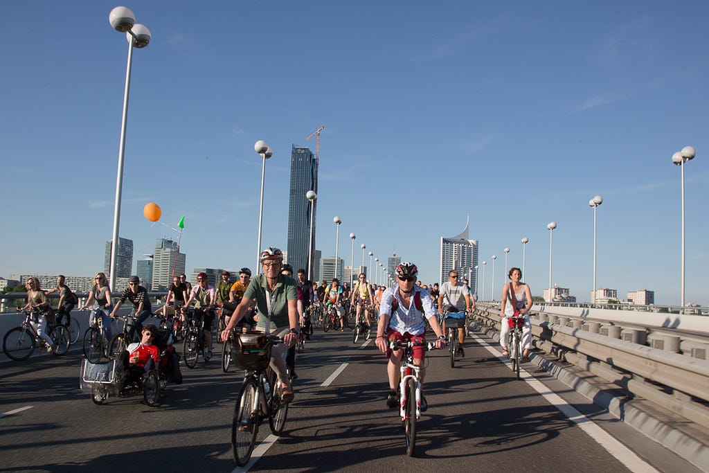 People cycling on a bridge, with skyscrapers in the background