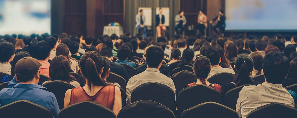 An audience listens to a speaker panel at an event.