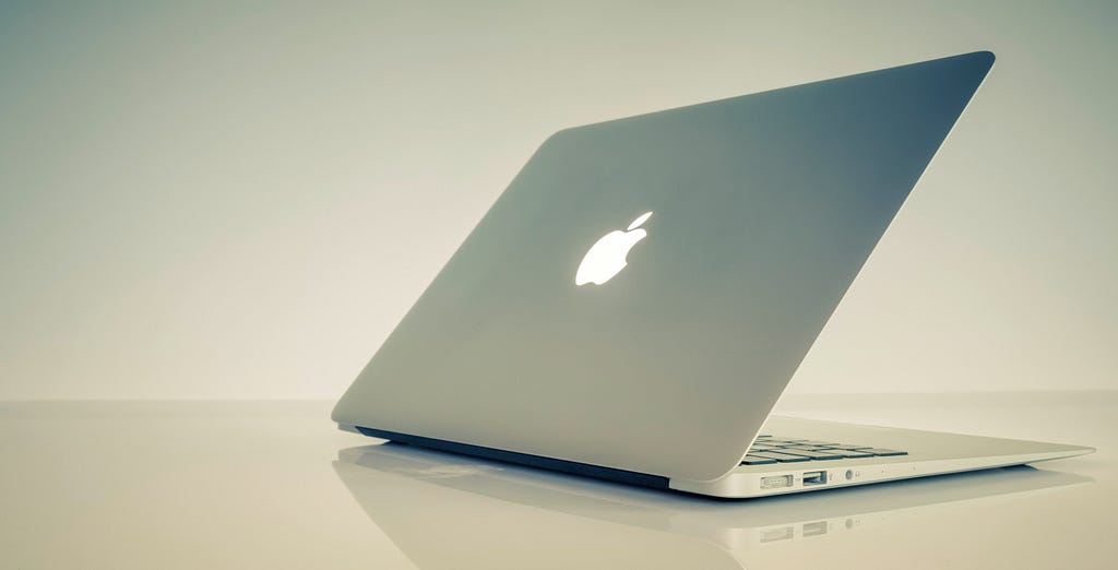 A MacBook Pro, cover partially opened, sits on a mirrored glass surface.