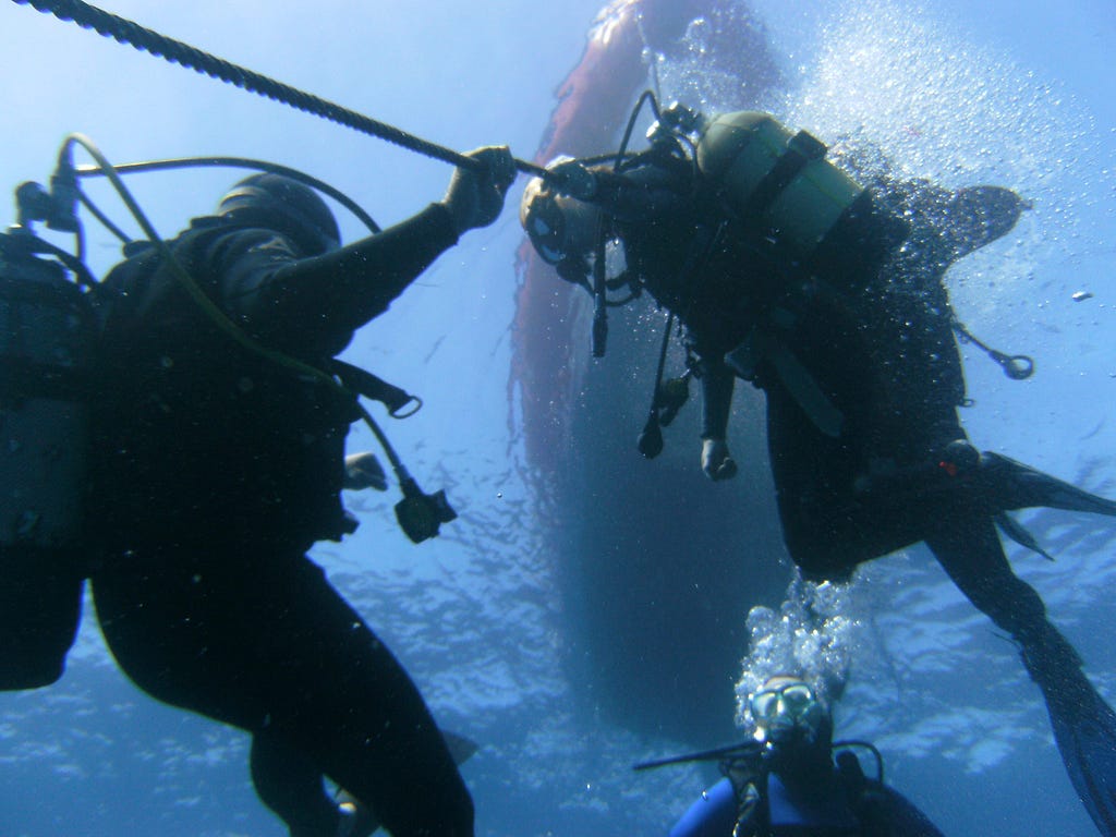 Two divers hold onto a rope underwater.
