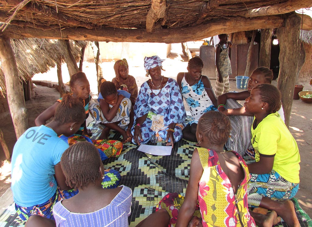 Grandmother Leader Egge facilitating a discussion with girls in the Kael Bessel village. The individuals are standing around a table.
