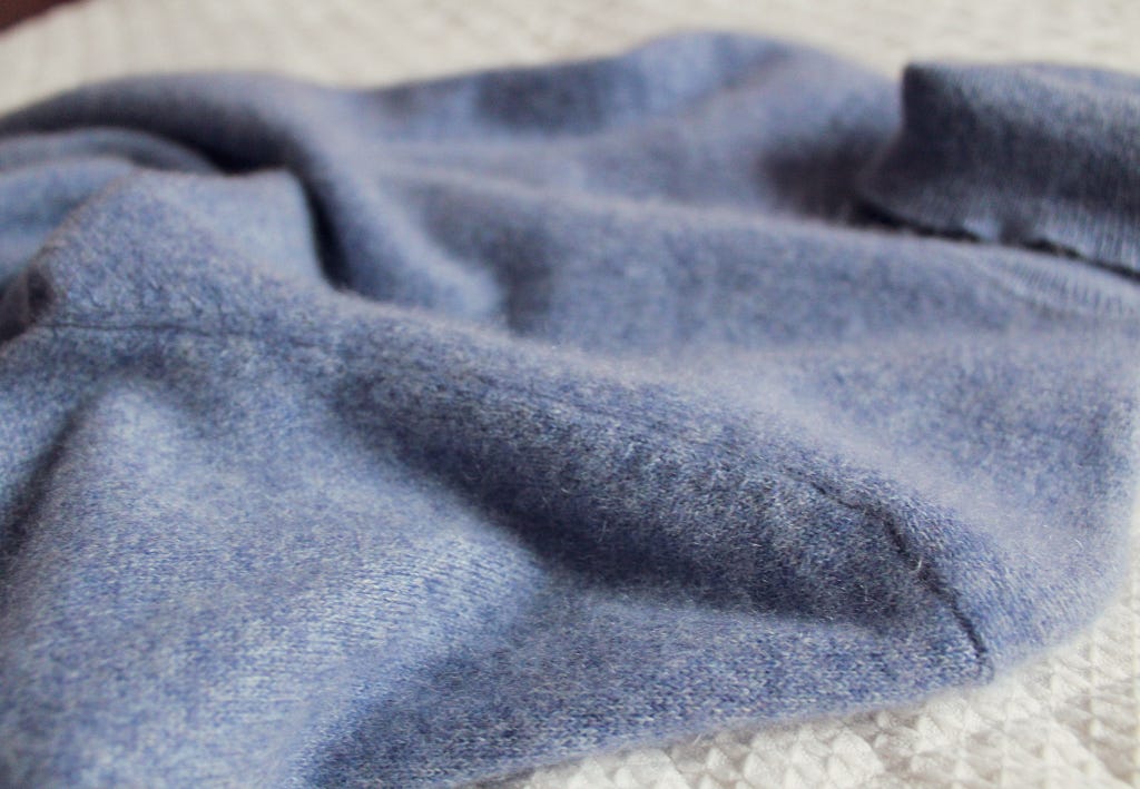 A light blue cashmere sweater laid out on a bed