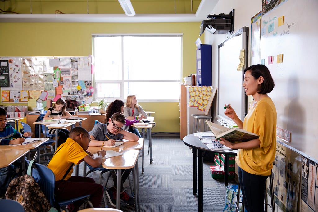 A teacher stands at the front of her classroom teaching her students. Photo by Hero Images/Getty Images