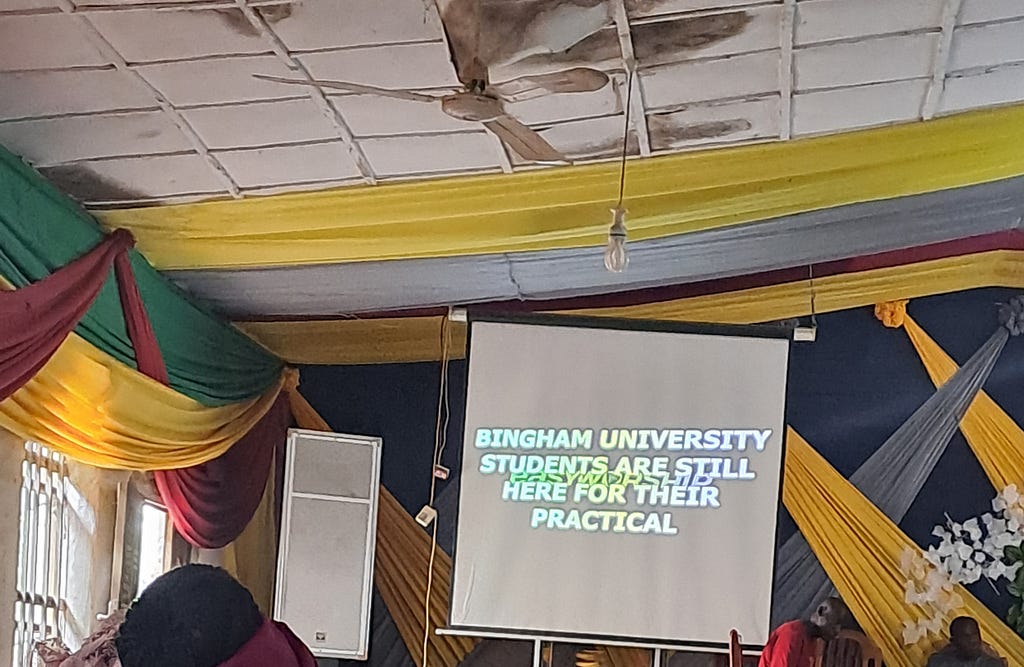 A lopsided projector projects the words “Bingham University students are still here for their practical”