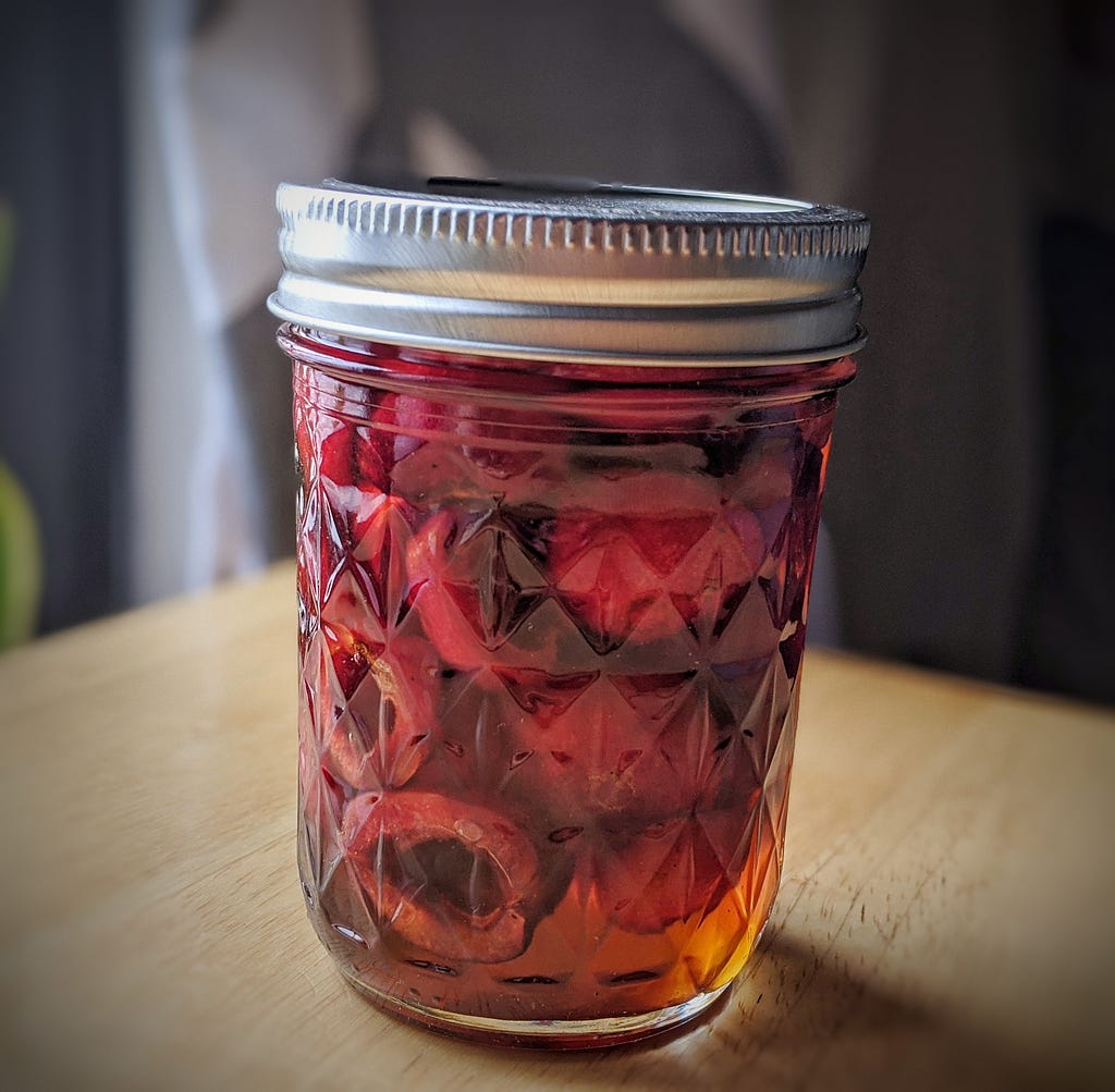 A mason jar filled with cherries and syrup.