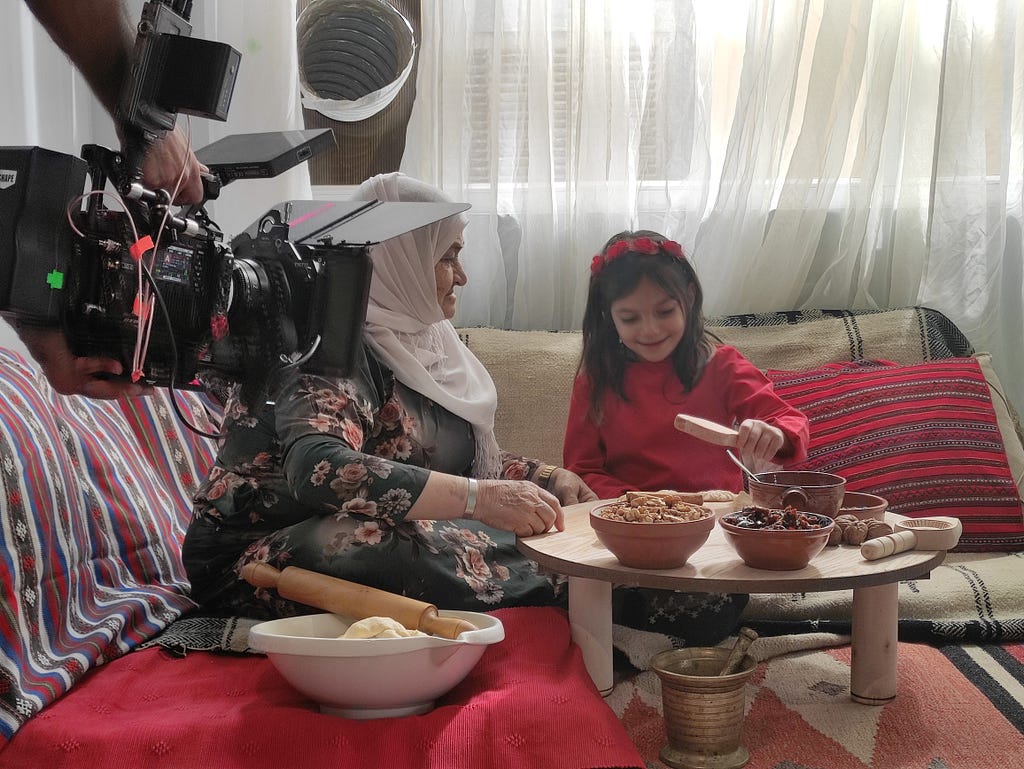 An elderly woman and a young girl seated around a round table preparing cookies.