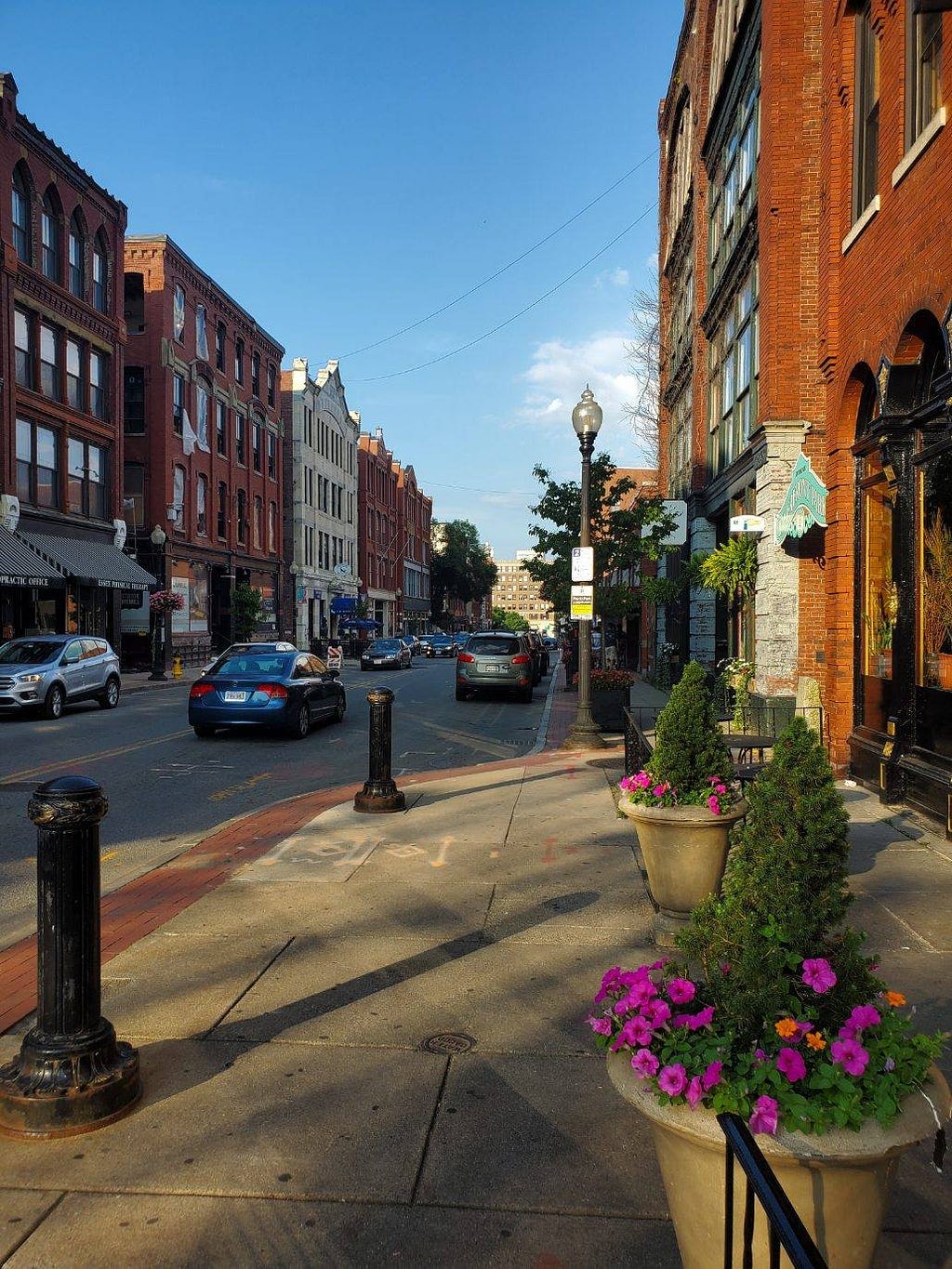 A main street with cars driving both ways, surrounded by brick buildings.