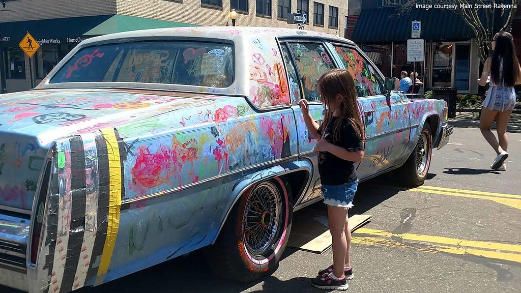 Young girl paints colorful patterns on old car at Main Street Ravenna’s Art on Main event.
