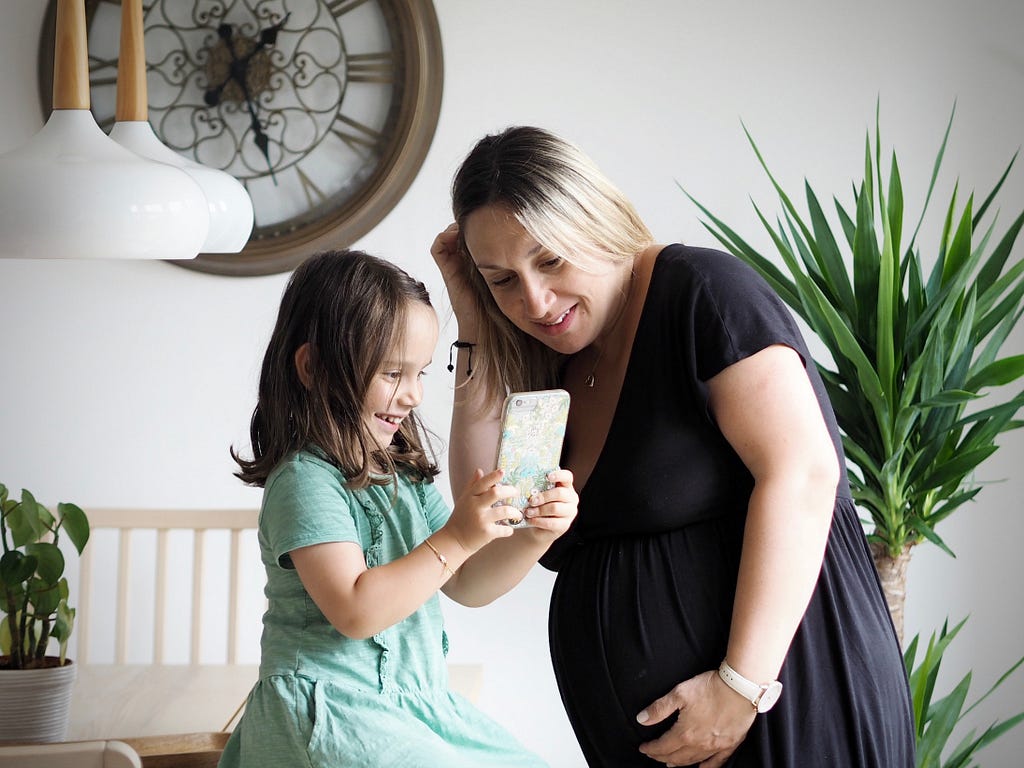 A pregnant mother and child look happily at a phone.