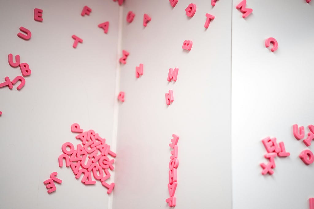 Pink magnetic plastic letters strewn around a folded piece of white card