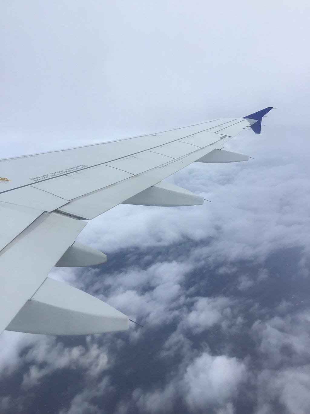 A gray plane wing against some white clouds with blue ocean far below