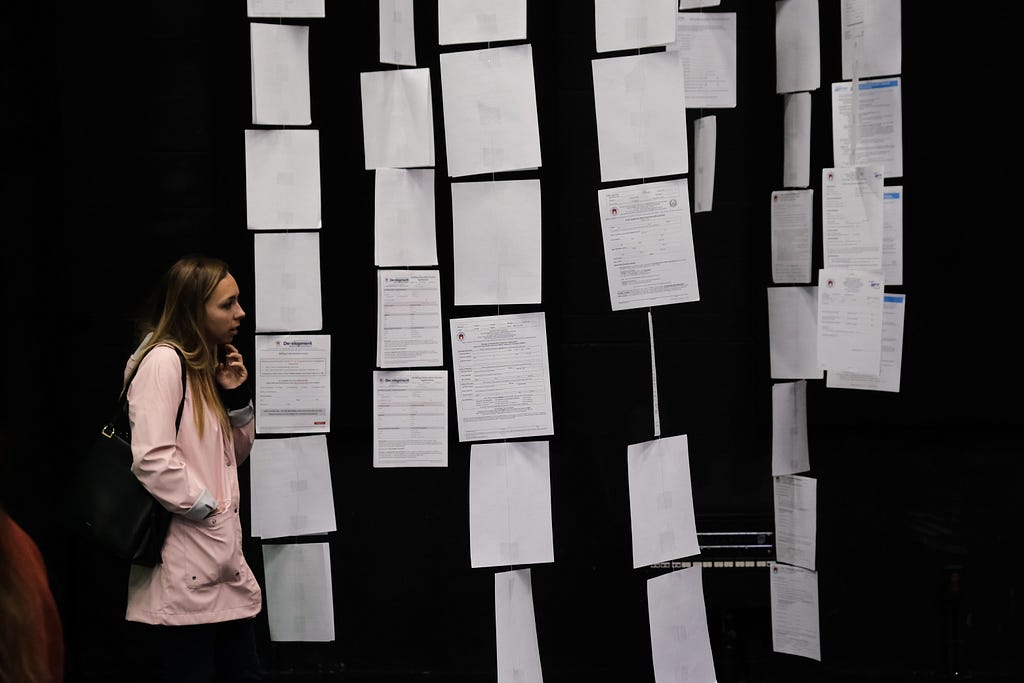 A women in a pink sweater looks at a row of forms along the back wall.