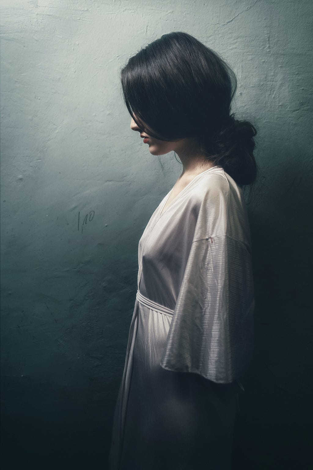 Black-haired woman silhouette in white silk robe against grey wall Becka Lynn