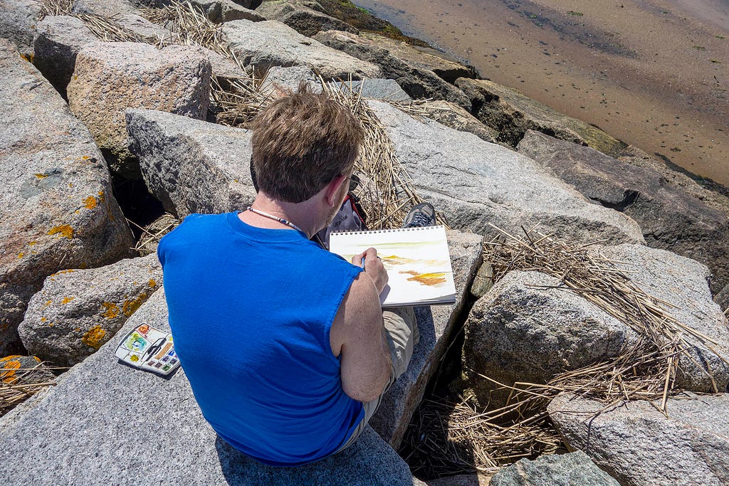 a guy sitting on a rock damn making a watercolor painting