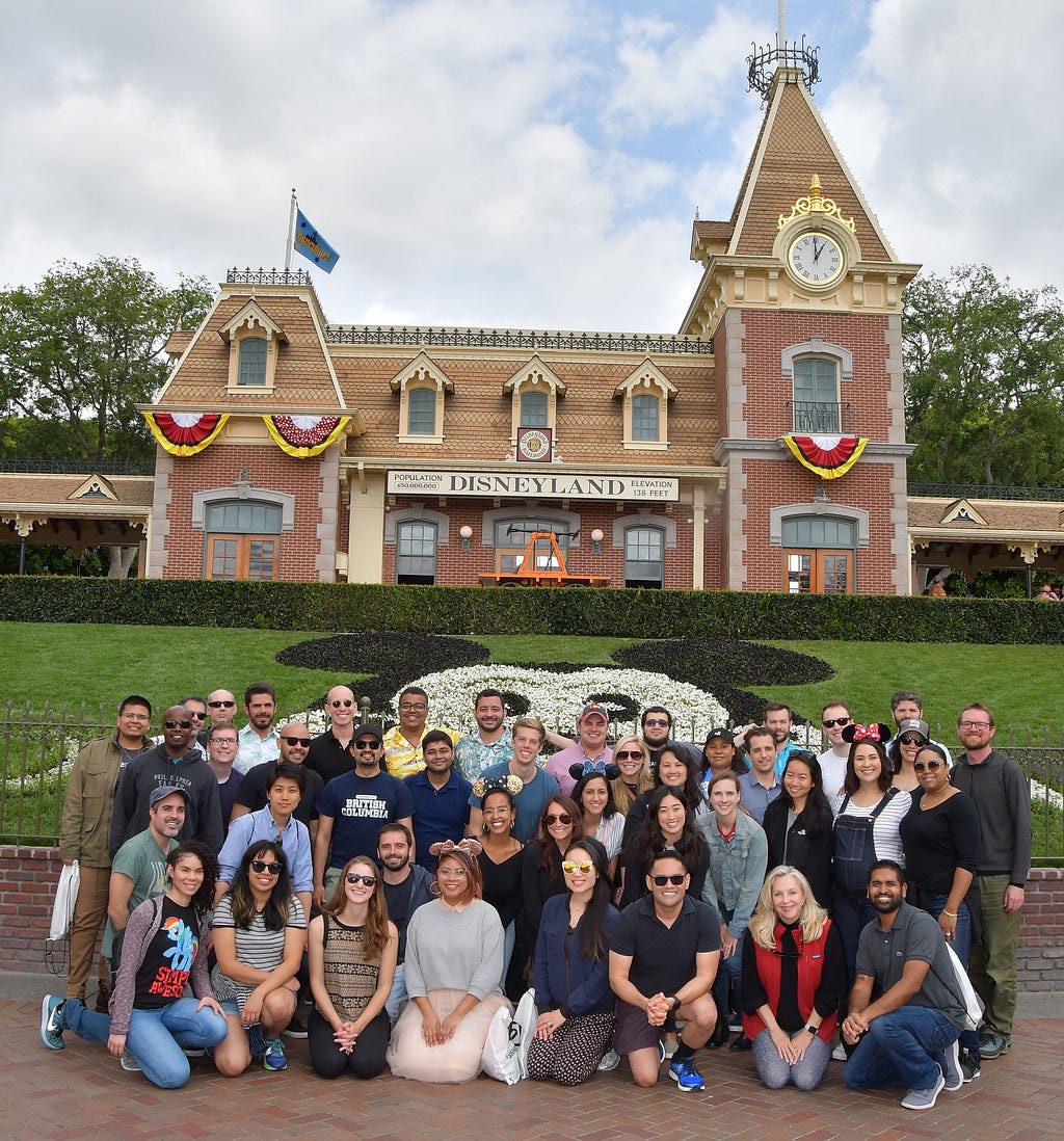 A group of people smiling, standing in front of a large mickey mouse face at Disneyland.