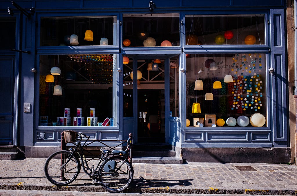 Picture of a blue storefront with windows and a bike outside, sitting on a stone sidewalk