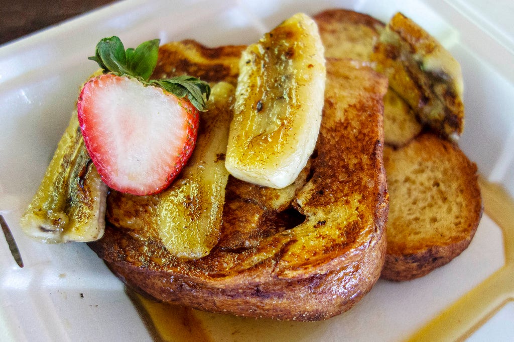 french toast with cut up bananas and a strawberry