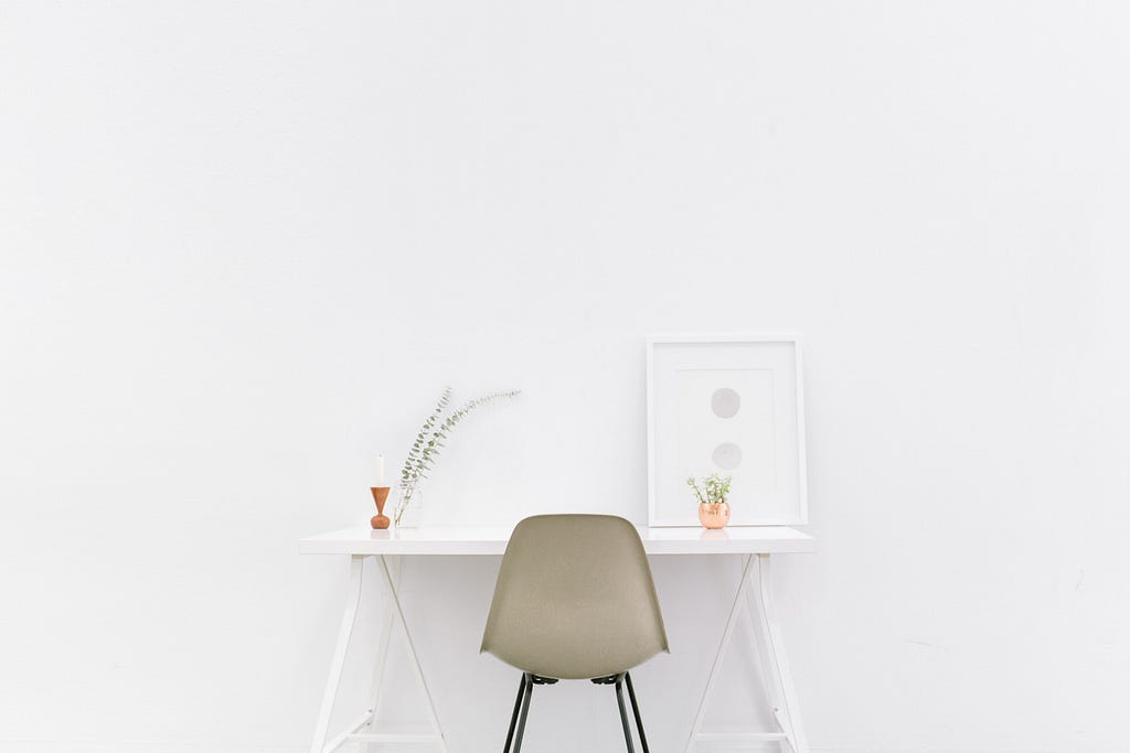 Super white office space with a framed painting and plants adorning the desk.