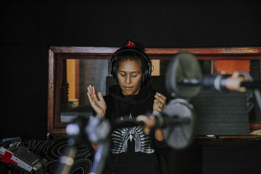 Kat in the music studio with head phones on, listening as she holds her hands up about to clap