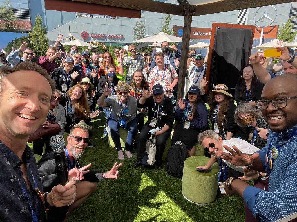 Photo taken outside on a sunny day at a Salesforce conference. It features Asterisk Loftis on the right and Adam Doti on the left foreground with about  thirty people smiling at the camera behind them.