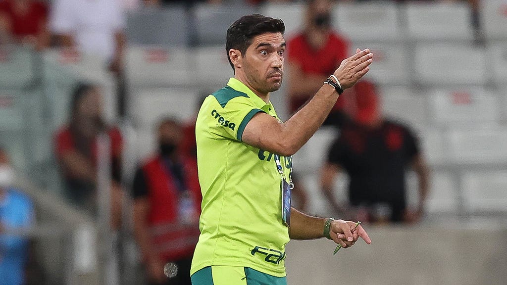 Abel Ferreira, técnico do Palmeiras, durante jogo contra o Athletico Paranaense pela Recopa Sul-Americana. Ele veste camisa verde limão e calça verde, mas aparece na imagem só da cintura para cima, com a mão direita levantada.