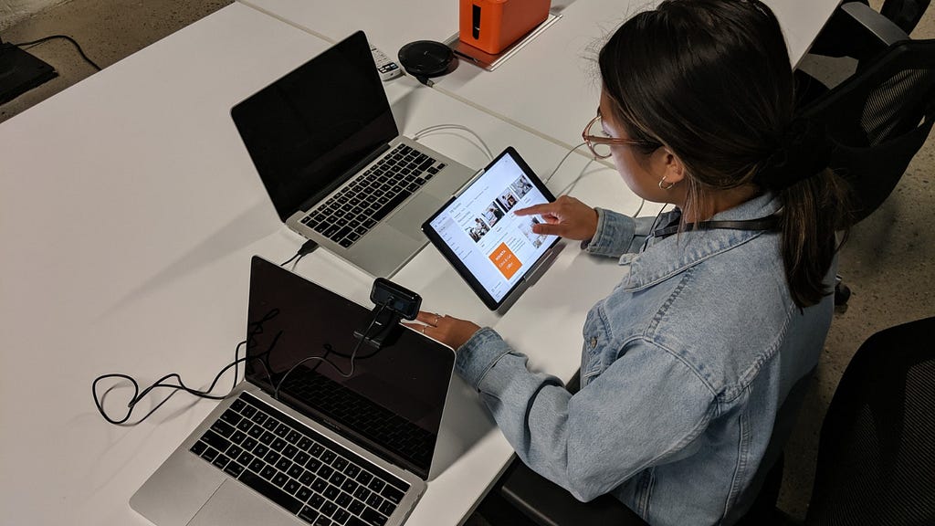 A person sitting down at a desk using a tablet with one laptop in front of them and one on their left side