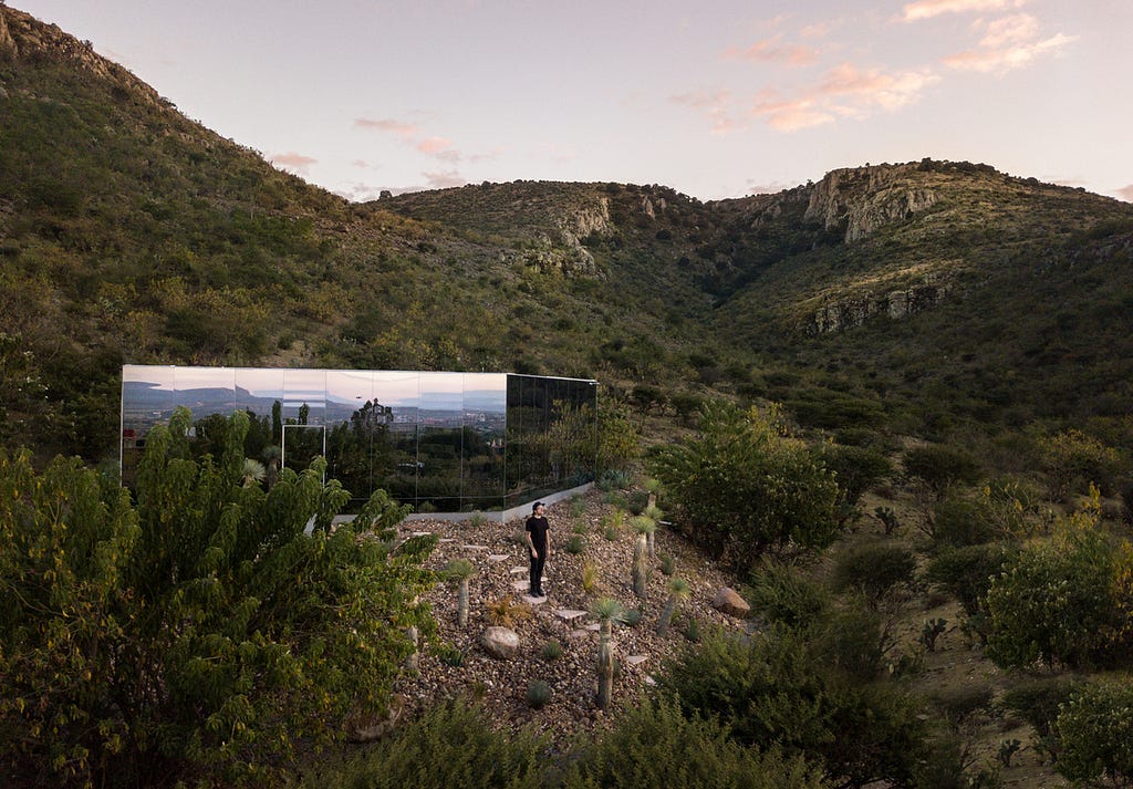 A single storey, mirror-clad building surrounded by green, volcanic landscape.