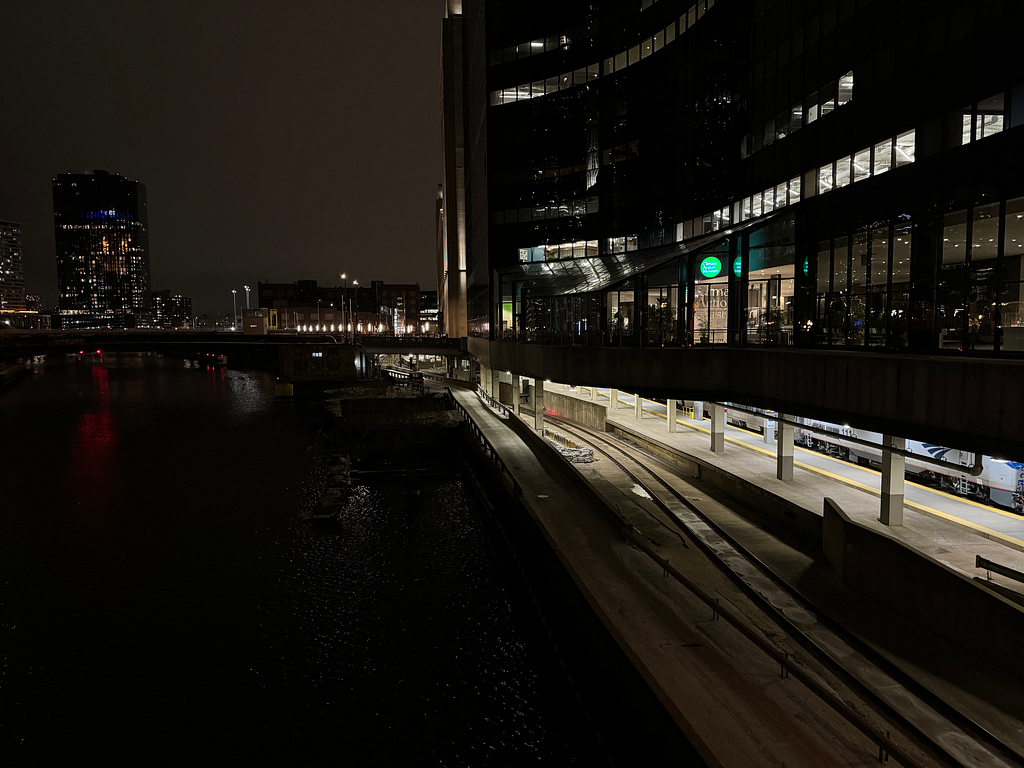 exterior photo showing the Climate Action Museum’s illuminated green sign at night. Below the museum level are Amtrak train station platforms (Union Station).