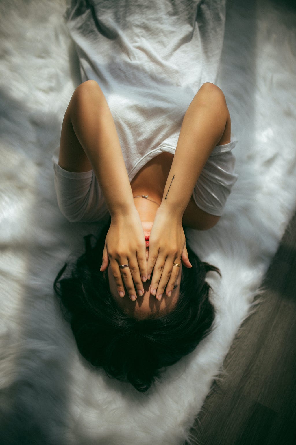 A woman lies on a bed, feeling sad, with her hands covering her face.