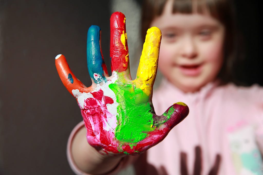 A young child with Down syndrome holding up their painted palm to show five painted fingers