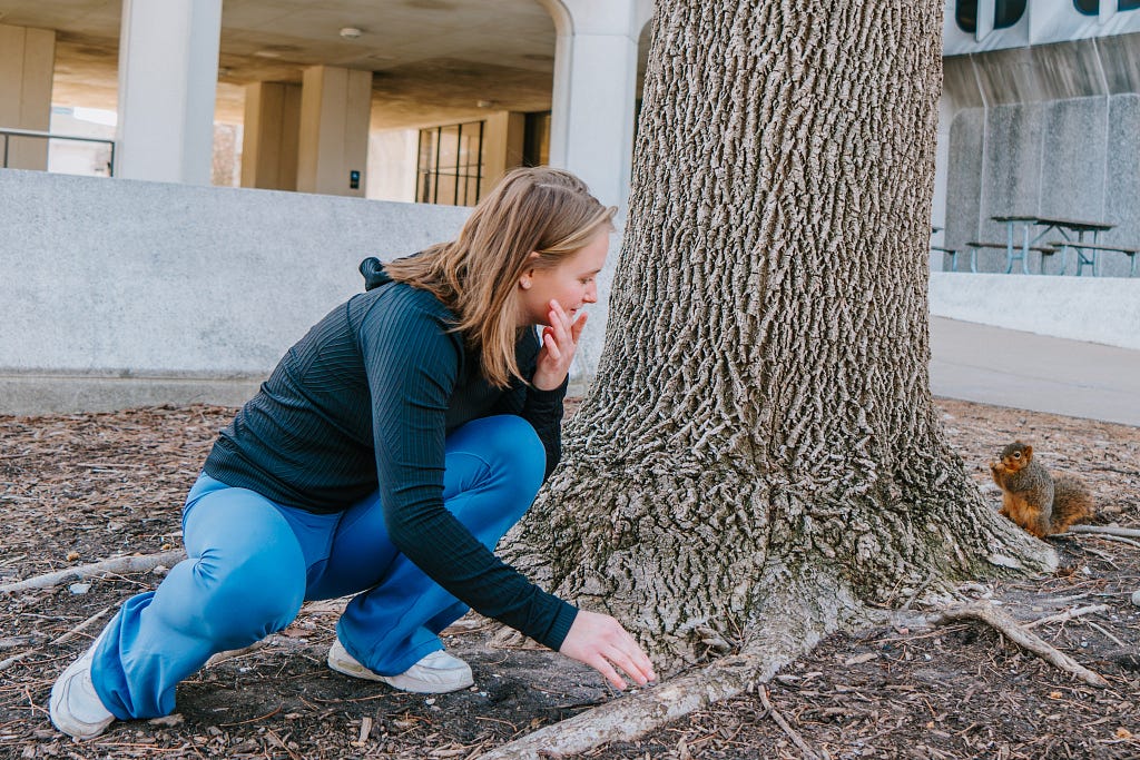 A student looks around a tree at a squirrel