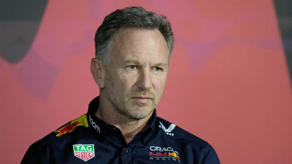 Christian Horner, in team uniform against a pink background, staring off camera with a face of grim disappointment.