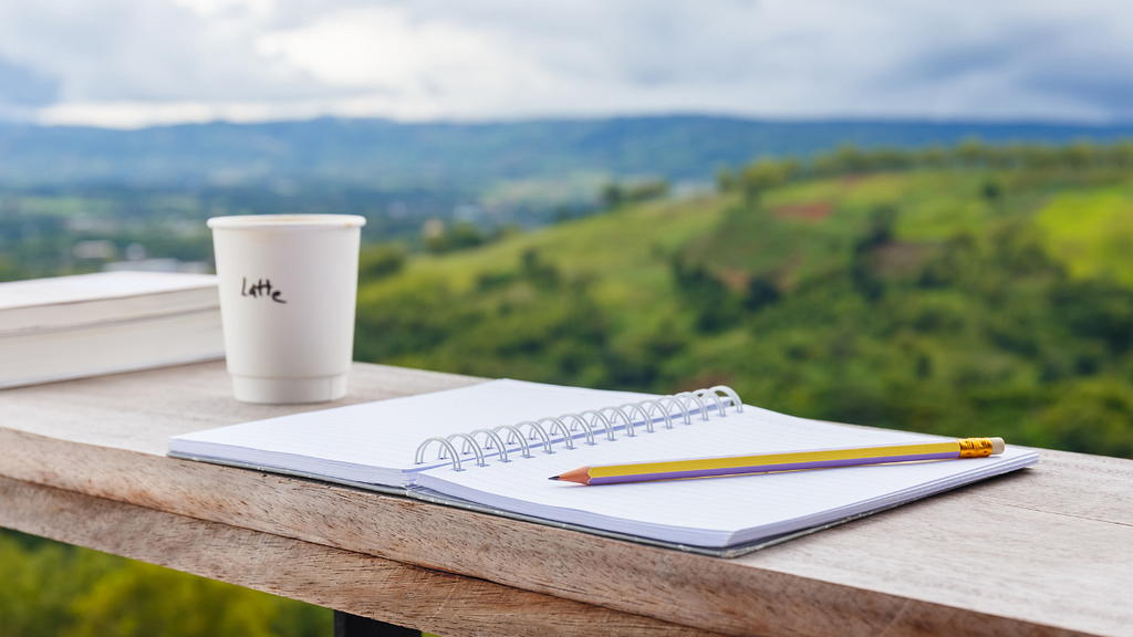 Outdoor writing. Coffe cup, open notebook and pencil on wooden table.