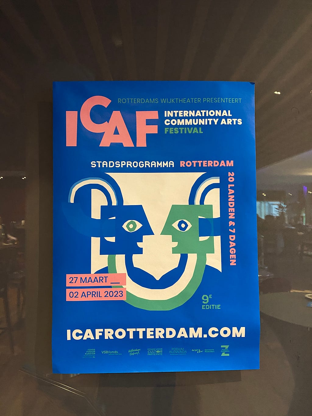 A poster for ICAF (International Community Arts Festival) in Dutch with an illustration of two figures looking at each other, connected through curves, on a blue background.