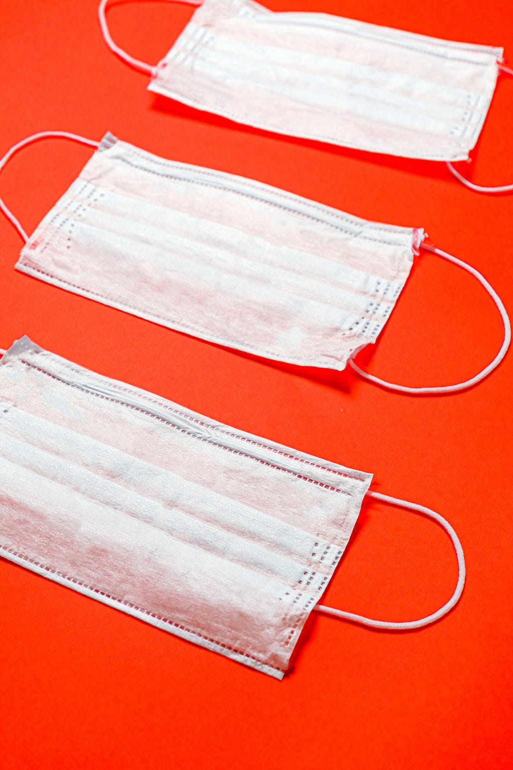 Photo of three white surgical face masks against a red background