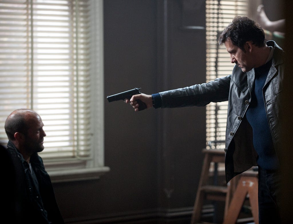 Clive Owen points a gun at Jason Statham in Killer Elite.